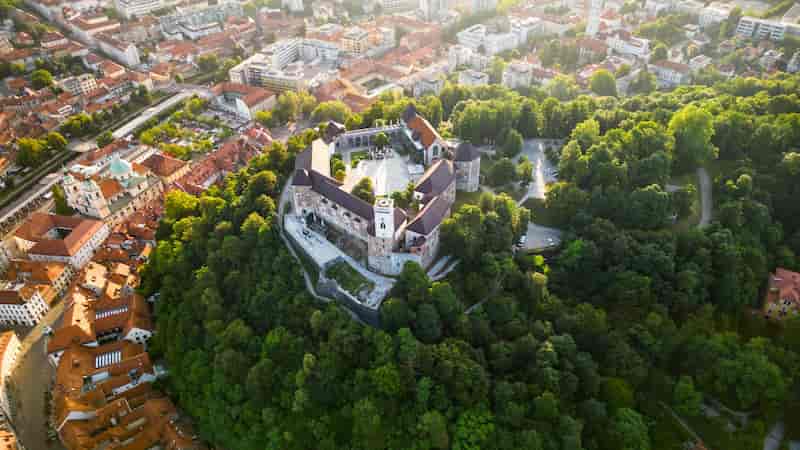 Aerial view of Ljubljana Castle surrounded by green forest and red-roofed old town buildings in Slovenia.