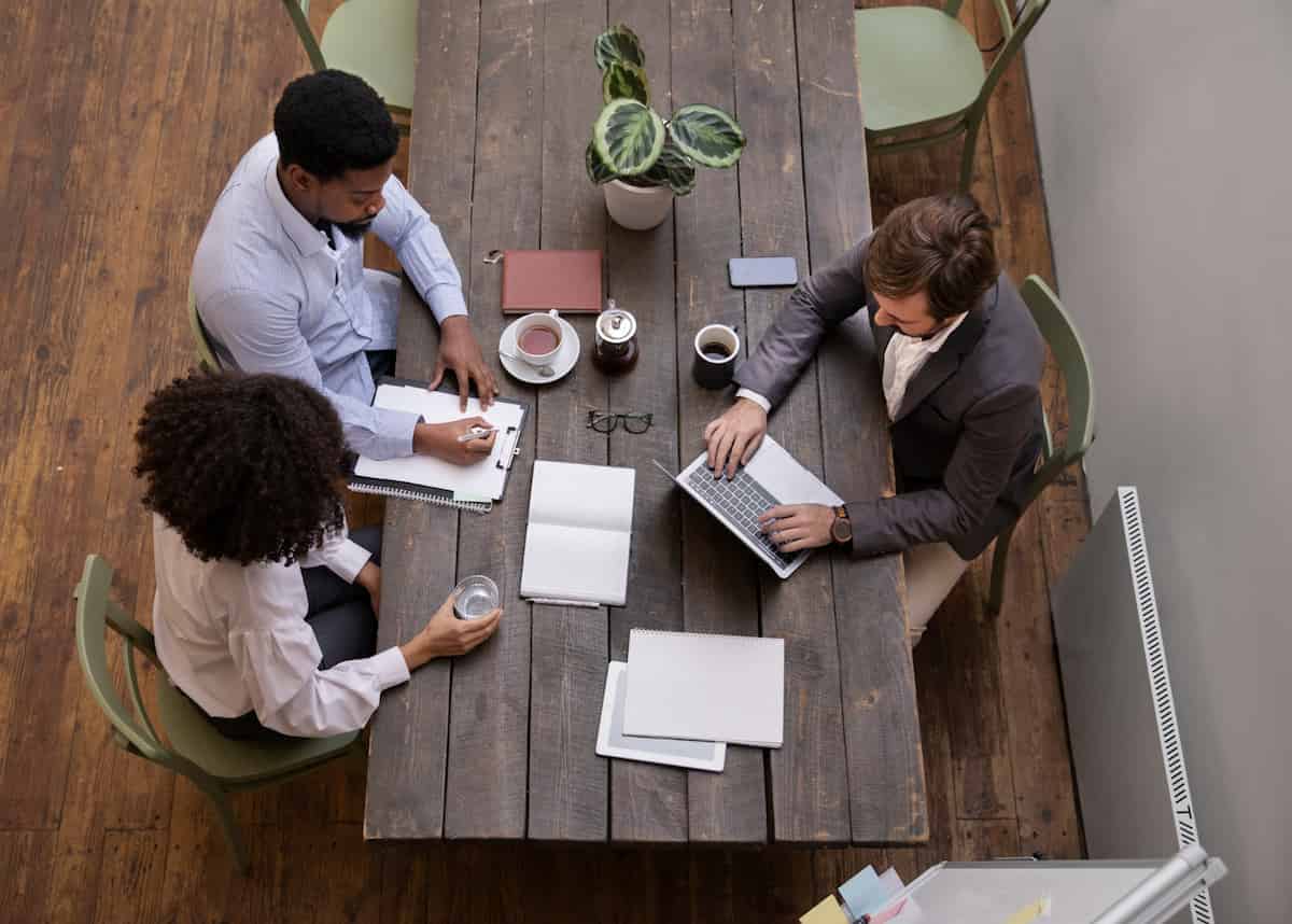 Overhead view of three people in a business meeting discussing documents and legal agreements around a wooden table