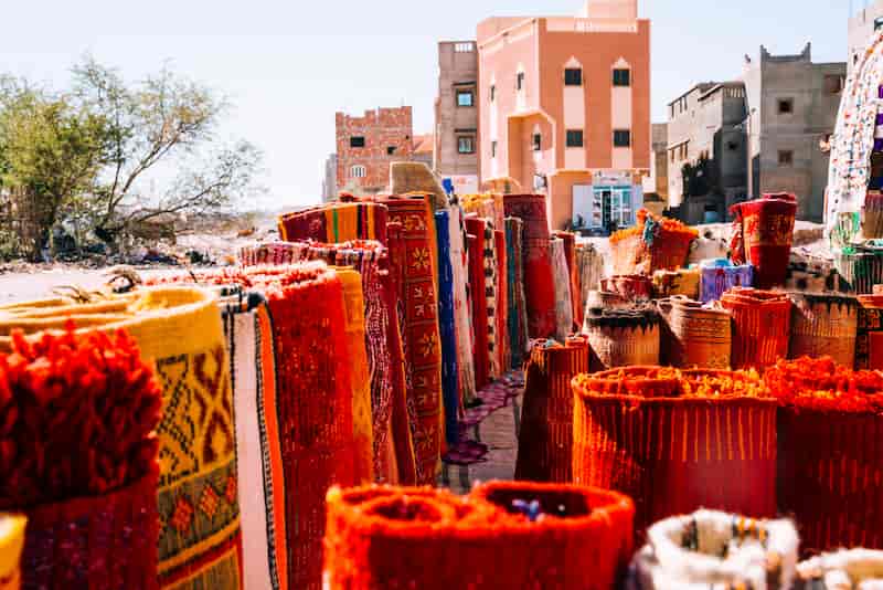 Brightly colored Moroccan rugs and woven baskets displayed at an outdoor market in Morocco.