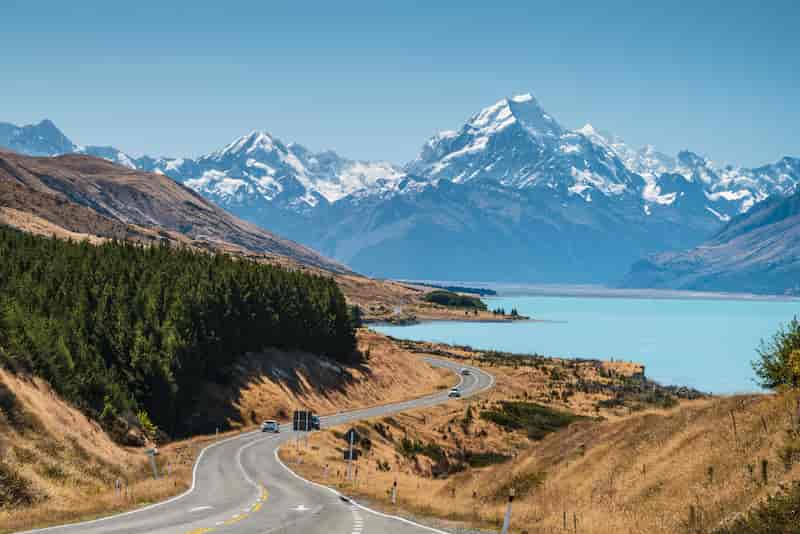 Scenic road leading to turquoise Lake Pukaki with snow-capped Aoraki / Mount Cook in the background, South Island, New Zealand.