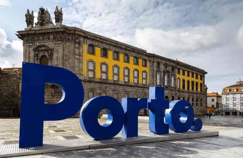 Large blue Porto city sign in front of historic stone buildings with yellow accents in Porto, Portugal.