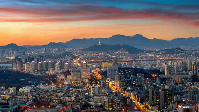 Seoul city skyline at sunset with Namsan Seoul Tower and mountains in the background, South Korea.