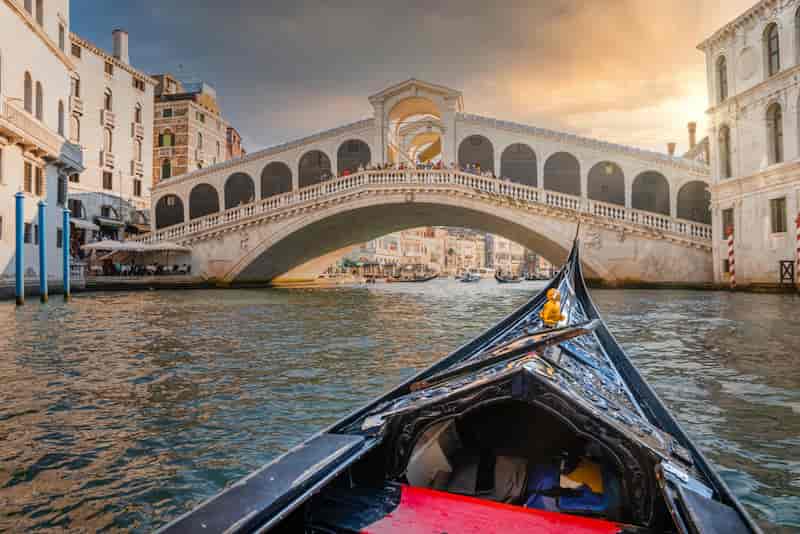 Gondola ride on the Grand Canal approaching the Rialto Bridge at sunset in Venice, Italy.