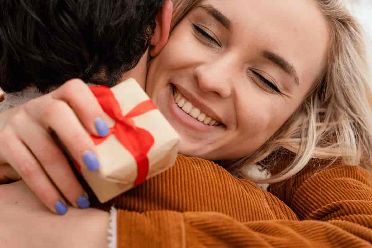 Smiling woman hugging someone while holding a small gift box wrapped in brown paper and tied with a red ribbon